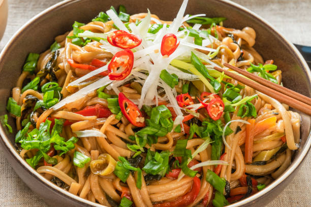 asian vegan lunch - spicy chow mein noodles with carrots, pepper and spinach with sliced radish, spring onions and chili peppers on a plate - bean vegetarian food stir fried carrot imagens e fotografias de stock