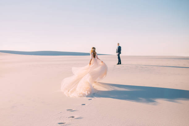 a woman runs to meet a man. dress with a very long hairpin that flies in the wind. photo from the back without a face. background desert at sunset. fine art photo - white wedding imagens e fotografias de stock