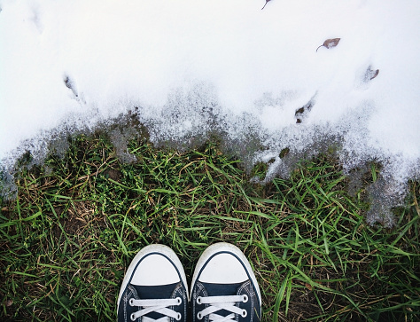 The beginning of spring. The boundary between the grass on the ground and white snow symbolizes the transition from winter to spring or from autumn to winter. Snow is melting. Sneakers on the grass.