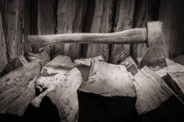 Hatchet axe and a pile of split wood logs used for fire. Concept with black and white colors- Axe viewed from the side.