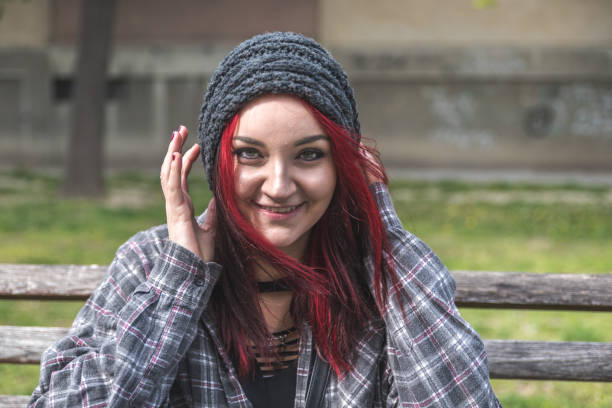 Positive smiling homeless red hair girl sitting on the bench on the street and looking in the camera  while she having fun stock photo