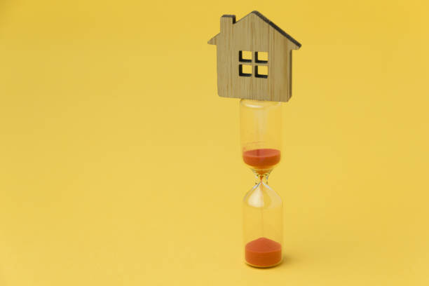 концепция инвестиций в недвижимость. песчаное стекло и миниатюрный дом - sand clock human hand hourglass стоковые фото и изображения