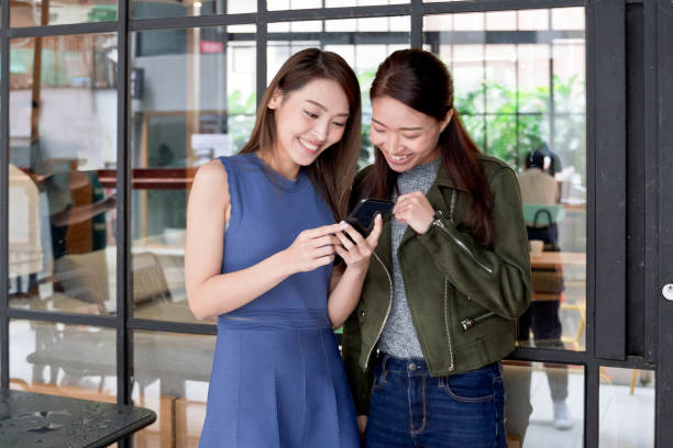 istock Two young asian friends reading a text message outdoors 1143936263