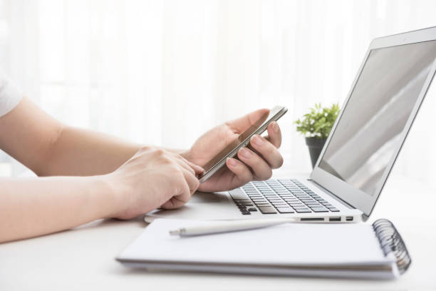 istock Hands using and touching smartphone screen over white office desk table with laptop and office supplies. Business concept. 1143939061