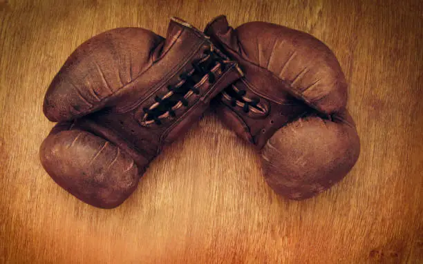 Photo of Boxing gloves. Old vintage retro pair of leather worn mittens are on the wood table. Red colors and soft lights. Gloves of retired boxer and fighter