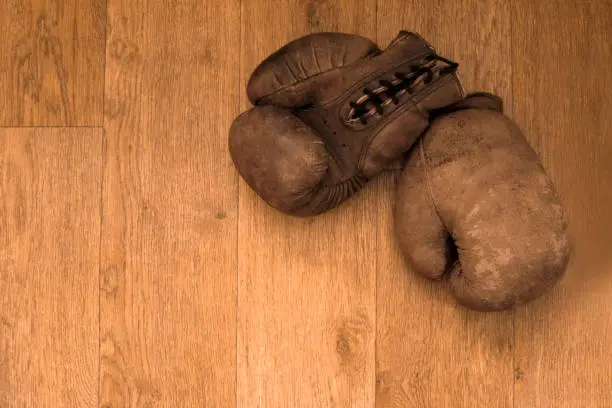 Photo of Boxing gloves. Old vintage retro pair of leather worn mittens are on the wood table. Red colors and soft lights. Gloves of retired boxer and fighter