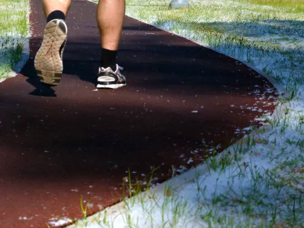 outdoor red rubber running track in spring with male runner's shoes close up view from behind showing sole of the shoe and muscular lower legs. intentional selective focus. sports and leisure concept.