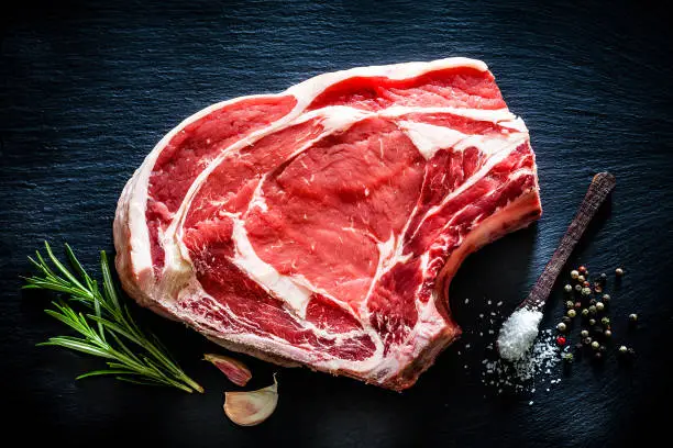Photo of Raw rib steak shot from above on black background
