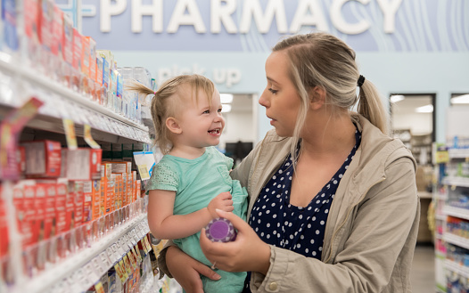 Concerned mother holding toddler and purchasing medicine in pharmacy