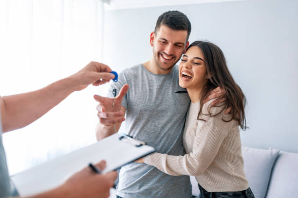 Happy couple is taking keys from their new house from broker and smiling. Happy couple is taking keys from their new house from broker and smiling. Hands of estate agent giving keys to the couple. The agent handed the keys a young couple real estate agent male stock pictures, royalty-free photos & images