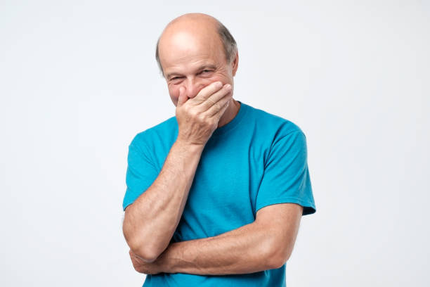 Senior man giggles and covers mouth with his hand Senior bald hispanic man giggles and covers mouth with his hand hysteria stock pictures, royalty-free photos & images