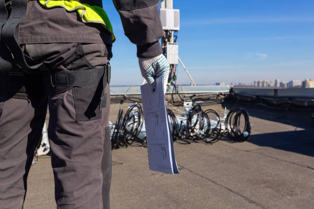 istock Professional industrial climber in helmet and uniform with  technical documentation in his hand and  antennas of GSM  DCS UMTS LTE bands, outdoor radio units  on the roof. Working process of upgrading telecommunication equipment 1143976012