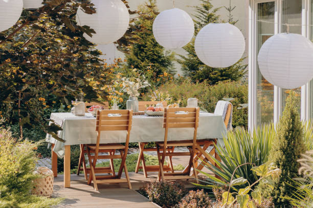 Real photo of round lamps above a table with wooden chairs in a garden Real photo of round lamps above a table with wooden chairs in a garden summer garden stock pictures, royalty-free photos & images
