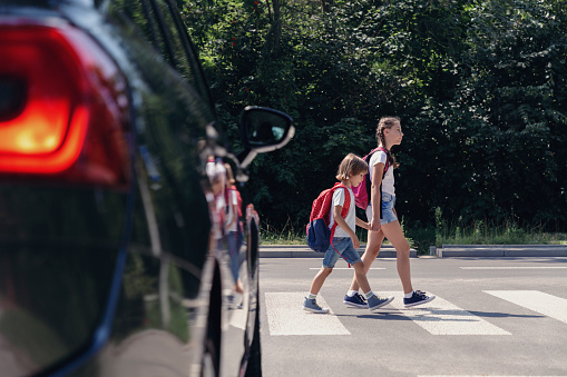 Los niños al lado de un coche caminando por el cruce peatonal a la escuela photo