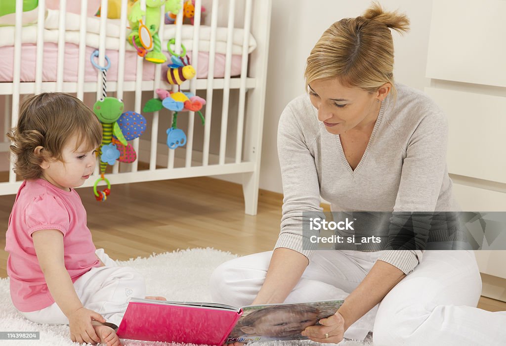 Madre mirando libro con su bebé niña - Foto de stock de 30-34 años libre de derechos