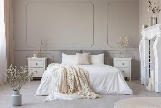 istock King size bed with white sheets and blanket between two wooden bedside tables flowers in vases 1143982948