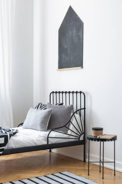 istock Cushions on bed next to table in black and white bedroom interior with blackboard on the wall and small metal bedside table, real photo with mockup 1143985049