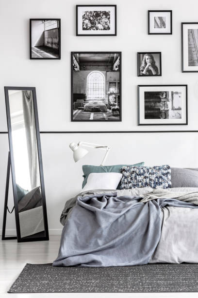 istock Mirror next to bed with grey sheets in white minimal bedroom interior with posters. Real photo 1143991805