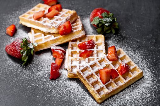 Belgium waffers with strawberries and sugar powder on black board background. Fresh baked wafers with copy space.