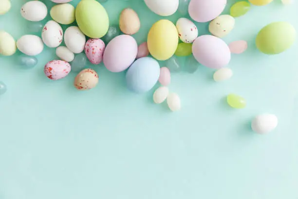 Happy Easter concept. Preparation for holiday. Easter candy chocolate eggs and jellybean sweets isolated on trendy pastel blue background. Simple minimalism flat lay top view copy space
