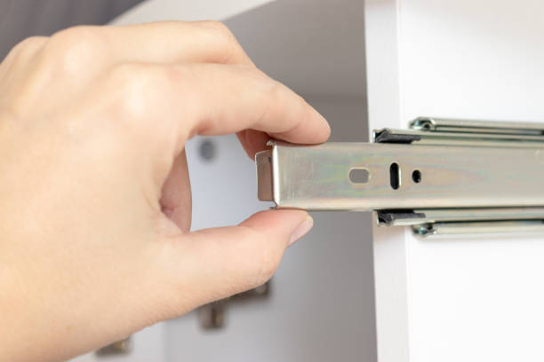 istock Assembling furniture from chipboard, hand holding roller guide of a drawer on white plank 1143998068