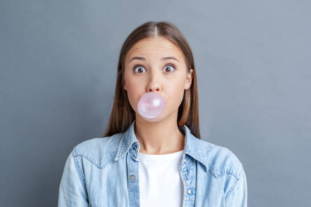 灰色で孤立した若い女性の自由スタイル - chewing gum ストックフォトと画像