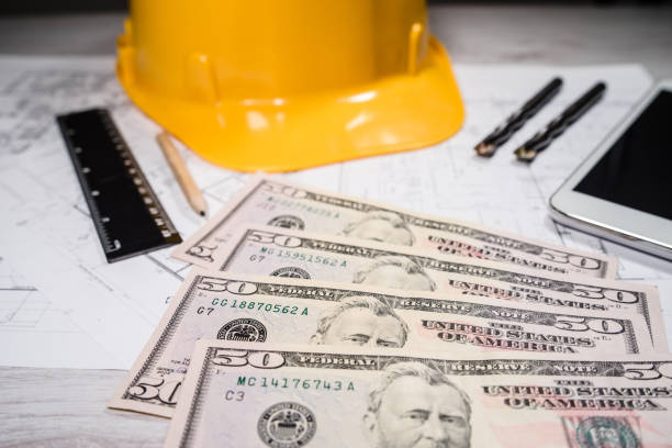 istock Construction industry costs money us dollars banknotes by tools safety equipment and blueprints 1144001007