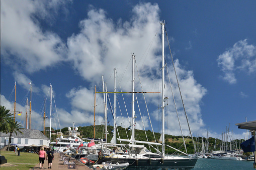 A senior couple walking down the quay at nelson’s dockyard in english harbor, antigua on a brilliant tropical january day.  A shirtless man works on one of the yachts and an incidental tourist wearing a backpack takes in the view.