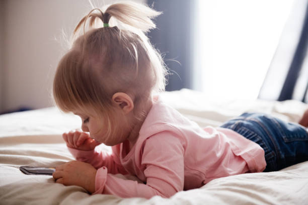 Cute little girl playing with cell phone on a bed stock photo