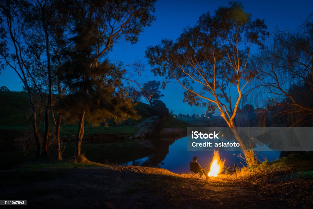 In de schemering een persoon zit bij een kampvuur aan de rand van het water, Yass, Australië - Royalty-free Australië Stockfoto