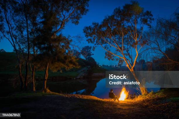 In De Schemering Een Persoon Zit Bij Een Kampvuur Aan De Rand Van Het Water Yass Australië Stockfoto en meer beelden van Australië