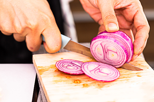 Close up Chef chopping a red onion with knife on the cutting board. Cutting the onion into slices.