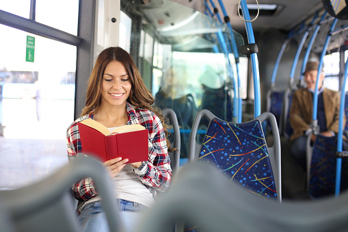 Young woman reading a book on a public bus. About 25 years old, Caucasian female.