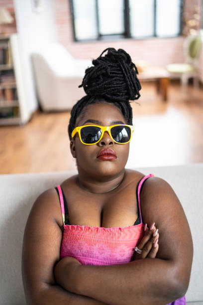 jeune femme africaine avec des lunettes de soleil jaunes s’asseyant des bras croisés - black hair photos et images de collection