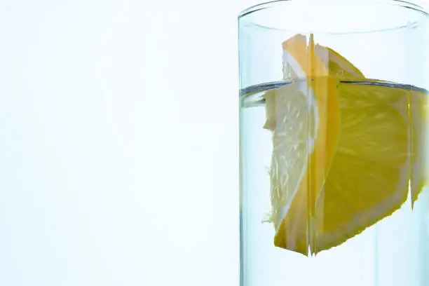 A slice of lemon in a glass of water on light background