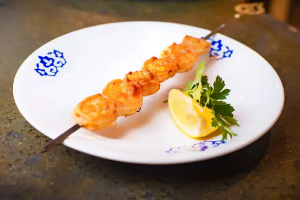 Grilled shrimp on a skewer with a slice of lemon and herbs on the plate