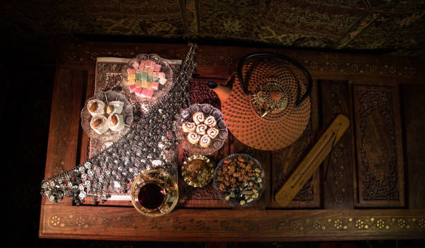 istock Arabian tea in glass with eastern snacks on vintage wooden surface. Eastern tea concept. Low light lounge interior with carpet. Empty space. 1144110005