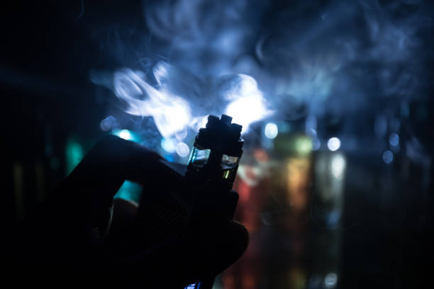 istock Vape concept. Electronic Cigarette vape explosion. Smoke clouds and vape liquid bottles on dark background. Light effects. Useful as vape advertisement. 1144110035