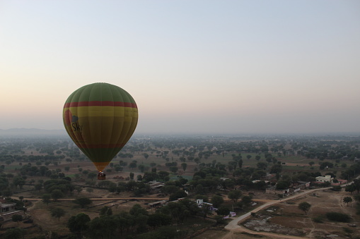 A yellow hot air balloon carrying tourists passes over rock formations in Goreme