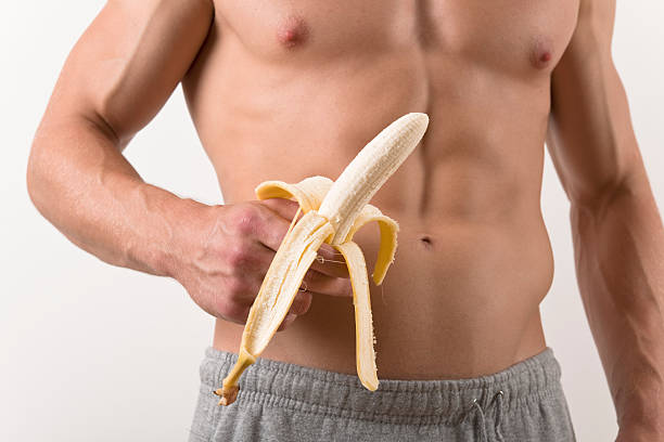 Shirtless muscular Man holding a peeled Banana Shirtless muscular Man holding a peeled Banana. phallus shaped stock pictures, royalty-free photos & images