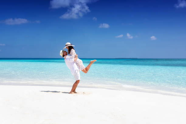 coppia in abiti estivi bianchi su una spiaggia tropicale - honeymoon foto e immagini stock
