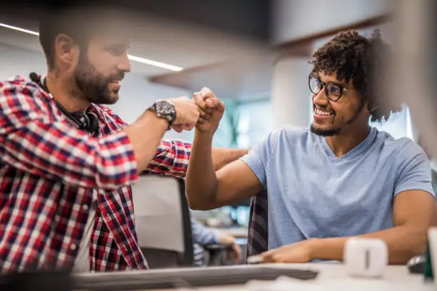 Happy male programmers supporting each other with fist bump in the office.