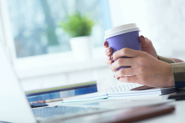 istock Morning coffee before a productive working day. Young female office worker holding coffee paper-cup and looking at the laptop screen while sitting at her working place in office. 1144133133