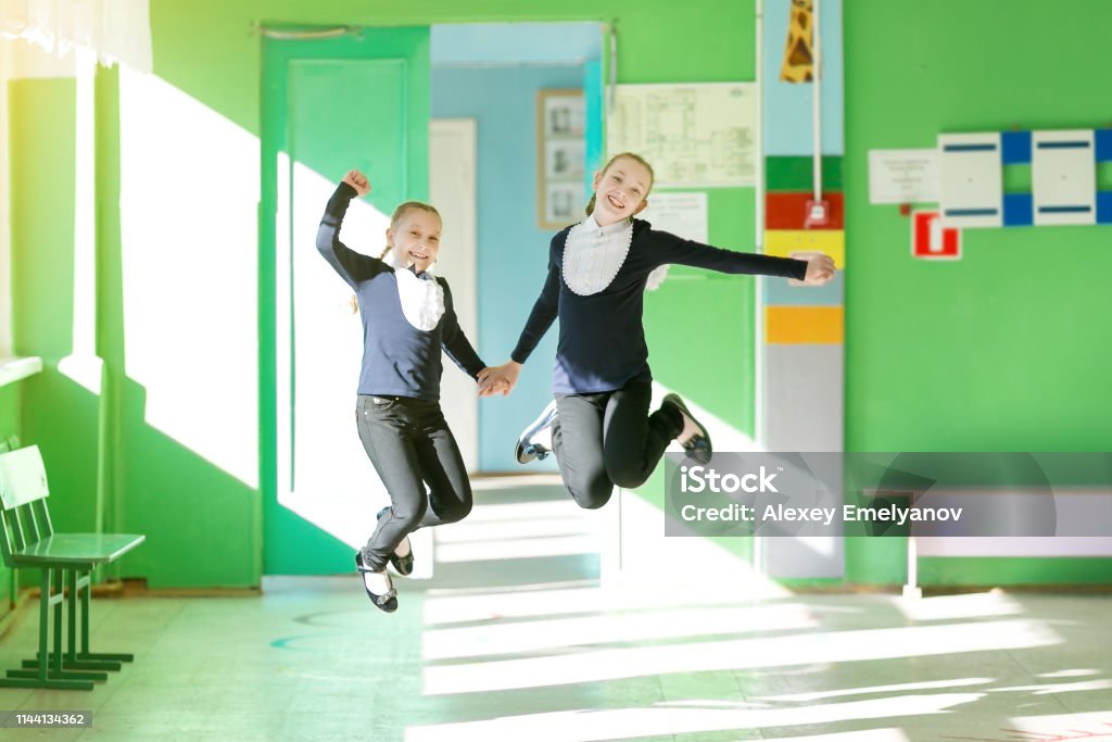 Dos colegialas saltan en el pasillo sosteniendo las manos. - Foto de stock de 10-11 años libre de derechos