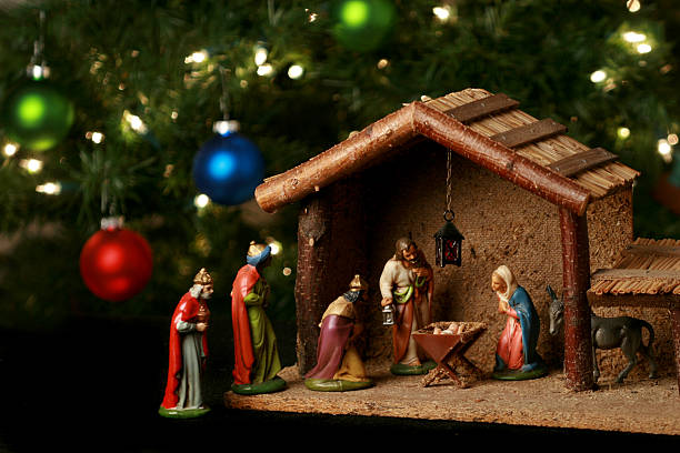 nativity scene next to a christmas tree - kerststal stockfoto's en -beelden