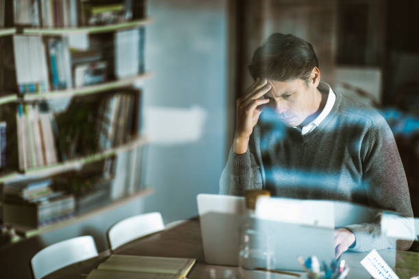 mid adult businessman reading problematic e-mail on laptop at home office. - looking through window businessman problems reading imagens e fotografias de stock