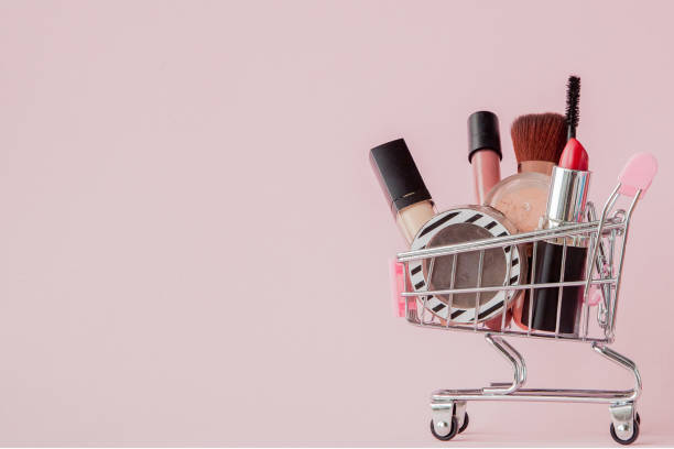 istock Creative concept with shopping trolley with makeup on a pink background. Perfume, sponge, brush, mascara, pencil, nail file, eye shadow, lip gloss in the basket, copy space 1144151585