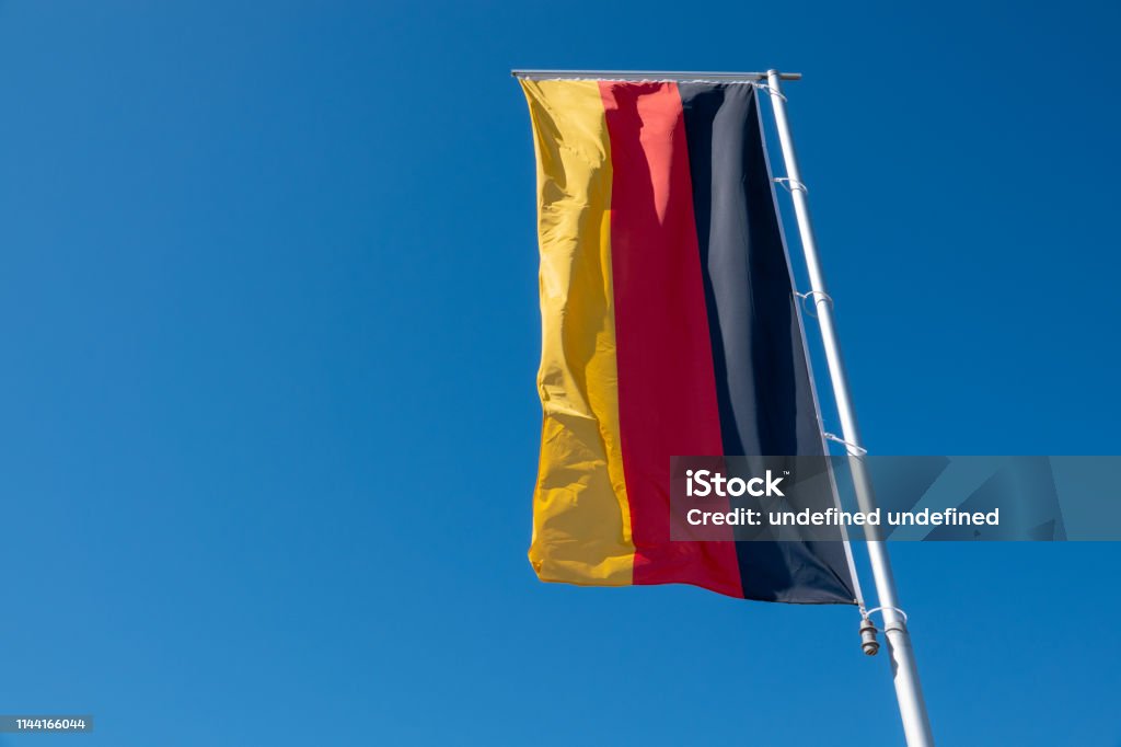 a German flag blows in front of a blue sky Allegory Painting Stock Photo