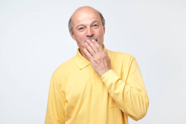 Mature bald man covering mouth and laughing. stock photo