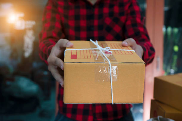 istock Delivery man in red uniform handing a parcel box over to a customer - courier service concep 1144169483